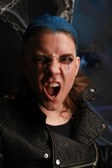 Teen alt boy with blue hair and shaved head dressed in black on dark background