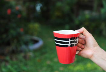 Closeup of a mug of hot coffee hold by woman's hand with natural background. 