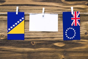 Hanging flags of Bosnia Herzegovina and Cook Islands attached to rope with clothes pins with copy...