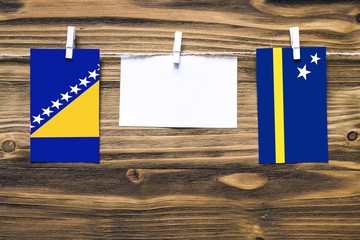 Hanging flags of Bosnia Herzegovina and Curacao attached to rope with clothes pins with copy space on white note paper on wooden background.Diplomatic relations between countries.