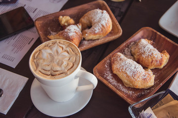 table with a cup of coffee with design next to some plates with croissants 