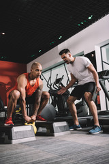 excited trainer shouting while motivating african american sportsman lifting weight