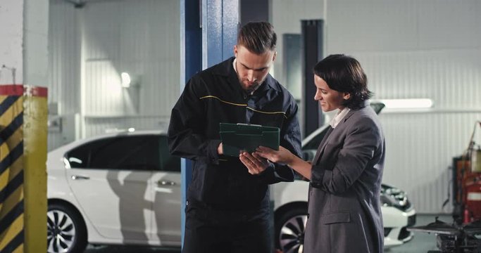 In a modern service auto charismatic mechanic man and beautiful business lady the owner of the machine analyzing the clipboard paper then going to the car