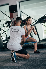 Fototapeta na wymiar back view of personal trainer controlling attractive sportswoman exercising with resistance band