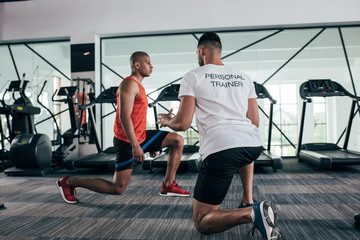 back view of personal trainer instructing african american sportsman exercising with resistance band