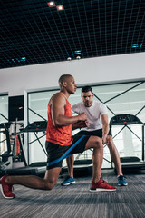 Fototapeta na wymiar attentive trainer controlling african american sportsman exercising with resistance band