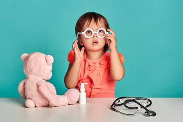 Smiling little girl play with stethoscope, spray for the throat and teddy bear. Studio shot