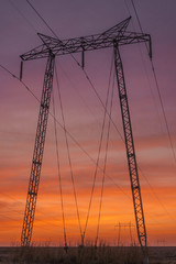 High voltage power towers standing strong in the rays of th e setting sun, under vivid colourful skies