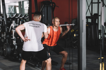 Fototapeta premium back view of personal trainer controlling young african american sportsman lifting barbell