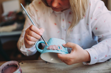 Woman working In her pottery studio. Ceramic workshop. Paint on clay mug in the pottery.