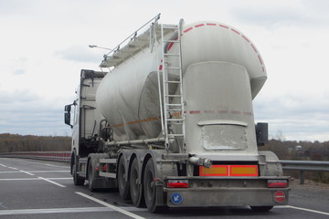 Cement truck with a round barrel semi trailer moving on asphalted highway road in autumn day, Logistics, bulk material road carriage, side rear view