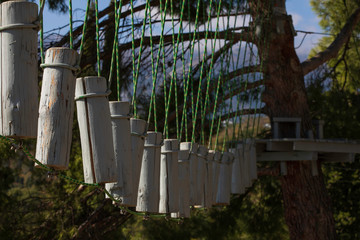 High rope course against forest and mountains. Vertical wooden bars tied to ropes and platform on pine, part of obstacle course in adventure park