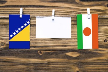 Hanging flags of Bosnia Herzegovina and Niger attached to rope with clothes pins with copy space on white note paper on wooden background.Diplomatic relations between countries.