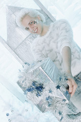 christmas blonde caucasian guy in white sweater with stars holding and opening gift present on the chair