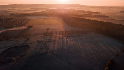 Aerial drone view of a forzen autumn nature landscape with forest and meadows. Contrast shadow and light by sunrise light. Harz Mountains