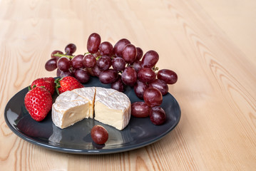 Soft Camembert cheese in a plate with berries on a wooden table