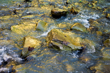 Reflection of sunlight on a mountain river with stones.