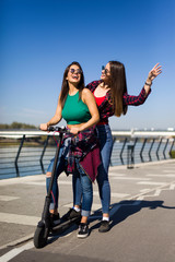 Pretty young female friends riding an electric scooter in the street