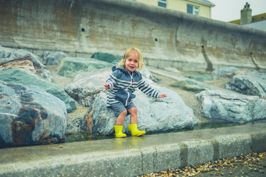 Little toddler running and playing on a rocky beach in the rain