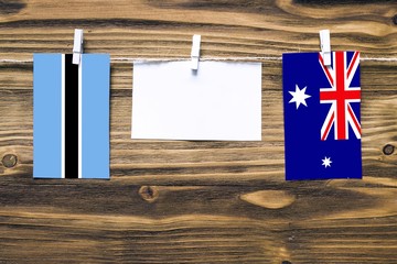 Hanging flags of Botswana and Heard and Mcdonald Islands attached to rope with clothes pins with copy space on white note paper on wooden background.Diplomatic relations between countries.