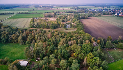 Aerial view of a forest, fields and meadows in front of a village in Northern Germany visible in the distance.