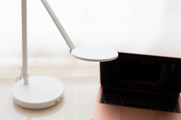 Modern rose gold laptop and white lamp on white desk