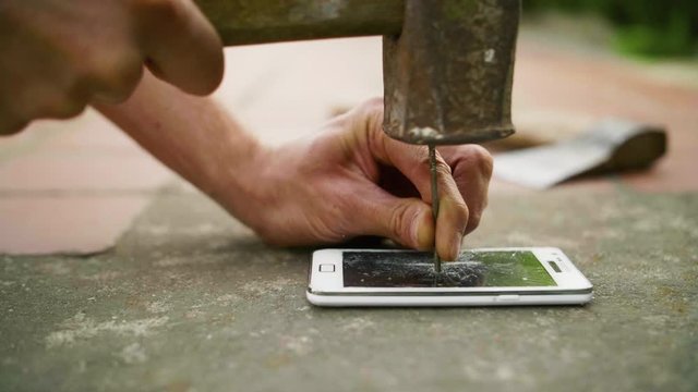 A man hammers a nail into the phone on the concrete ground in slow motion