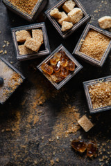Flat lay composition with different types of sugar on dark background.
