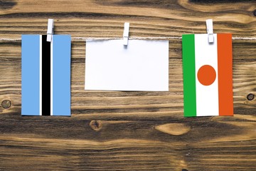 Hanging flags of Botswana and Niger attached to rope with clothes pins with copy space on white note paper on wooden background.Diplomatic relations between countries.