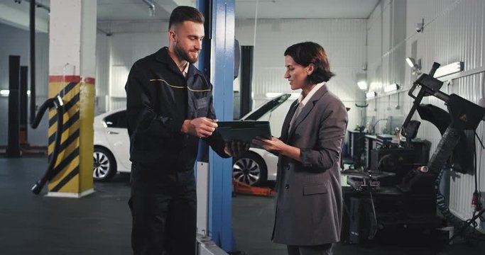 Mature mechanic guy and attractive lady sign some documents before going to the car to check the problem in a auto garage
