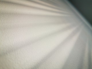 Obraz premium The shadow of the blinds on a white wall. Abstract monochrome pattern. The rays of reflected sun rays.