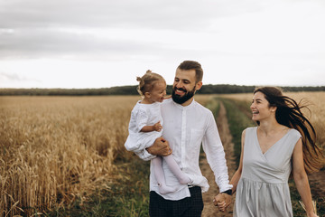 happy family on the walk in the wheat field: Father and a cute young wife with her little daughter happy parents with her baby