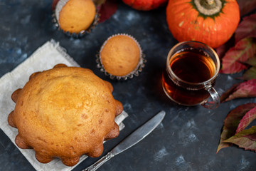 Big tasty cupcake for the holiday. Nelouin with pumpkin. Nearby is a transparent cup of hot, black tea. On a dark background. 
