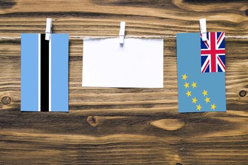 Hanging flags of Botswana and Tuvalu attached to rope with clothes pins with copy space on white note paper on wooden background.Diplomatic relations between countries.