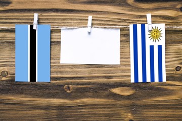 Hanging flags of Botswana and Uruguay attached to rope with clothes pins with copy space on white note paper on wooden background.Diplomatic relations between countries.