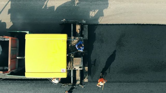 People lay asphalt on a road, using shovels. Aerial view of roadworks.
