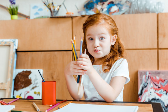 cute redhead kid holding color pencils in art school