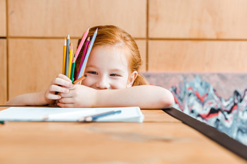 selective focus of smiling redhead child holding color pencils