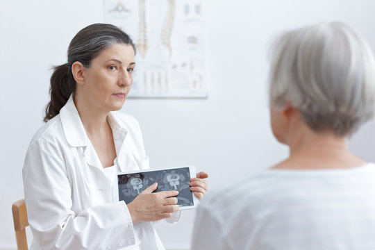 Female doctor with tablet computer showing her senior patient cat scan images of her degenerated vertebrae.