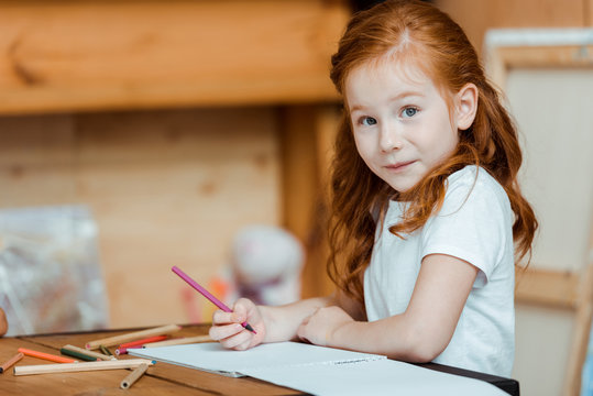 cute redhead child holding color pencil and looking at camera