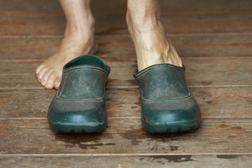 Barefoot woman puts rubber boots on standing on a wooden floor