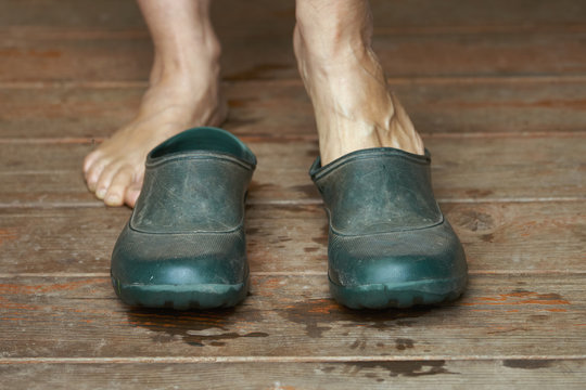 Barefoot Woman Puts Rubber Boots On Standing On A Wooden Floor