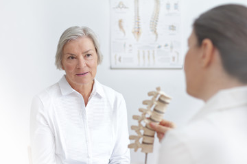 Aging and back pain concept: doctor of rheumatolgy showing her senior patient a slipped disk on a backbone model.