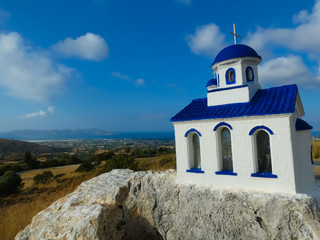 Small orthodox church on a white and blue stone with the background of the landscape and the sea