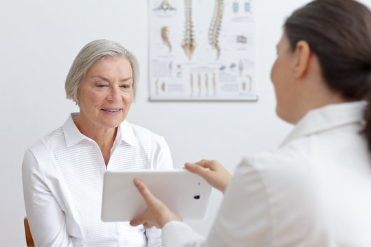 Health care technology concept: general practitioner showing her smiling senior patient lab results on a tablet pc.