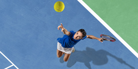 Young caucasian brunette woman in blue shirt playing tennis at the court. Hits ball with racket, outdoors. Youth, flexibility, power, energy. Copyspace. Top view. Motion, action, healthy lifestyle.
