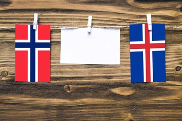 Hanging flags of Bouvet Islands and Iceland attached to rope with clothes pins with copy space on white note paper on wooden background.Diplomatic relations between countries.