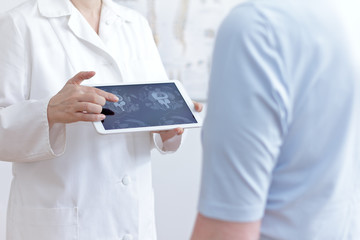 Back pain concept: doctor with tablet pc showing her patient cat scan images of her lumbar spines.