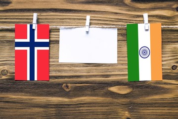 Hanging flags of Bouvet Islands and India attached to rope with clothes pins with copy space on white note paper on wooden background.Diplomatic relations between countries.