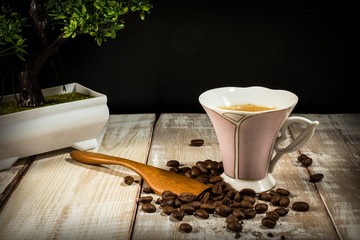 cup of coffee, spoon, coffee beans on a wooden table with bonsai